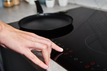 Modern kitchen appliance. Woman hand turn on induction stove to cook. Finger touching sensor button...