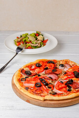 Vegetable salad with roasted meat and cheese and Sliced whole salami pepperoni pizza on a wooden table.