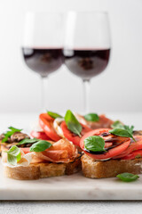 Bruschetta set with prosciutto and basil, tomatoes and mozzarella, camembert and berries, mushrooms and parsley on marble board. Antipasto open sandwich appetizer