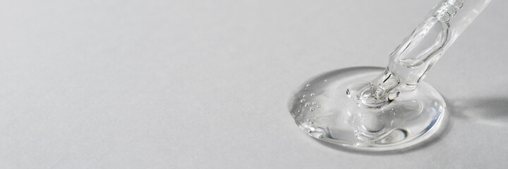Drop of facial serum with bubbles pouring from transparent pipette on grey background. Web banner...