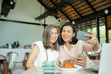 women meeting in cafe. friends taking photo on phone. beautiful smiling girlfriends having coffee break and taking selfies on mobile phone in coffee shop. Two girl friends drinking coffee.
