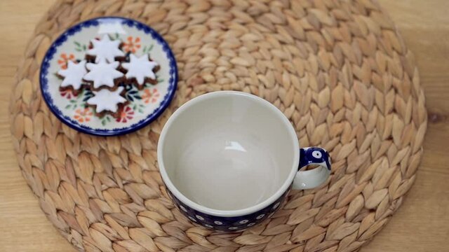 Eine Hand gießt kochendes wasser in eine Teetasse mit Teebeutel. Weihnachtliche Stimmung mit Gebäck. Zimtsterne liegen auf einem kleinen Teller im Hintergrund. Viele Platz für Text. Selektive Schärfe