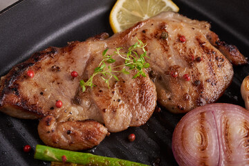Grilled pork steak from a summer BBQ served with Vegetables, asparagus, baby carrots, fresh tomatoes and  spices. Grilled steak on  Grill pan on stone background. top view.