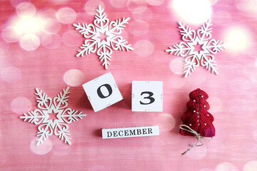 Calendar for December 3: cubes with numbers 0 and 3, the name of the month in English, decorative snowflakes and a Christmas tree on a pink background, bokeh
