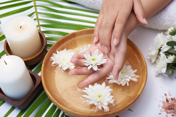 Fototapeta na wymiar Woman soaking her hands in bowl of water and flowers, Spa treatment and product for female feet and hand spa, massage pebble, perfumed flowers water and candles, Relaxation. Flat lay. top view.