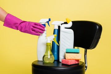 cropped view of cleaner reaching bottle with detergent near clean sponges on black chair isolated on yellow