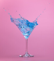 Blue liquid splashing out of martini cocktail cup isolated on pastel pink background