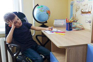 Back to school. Little tired boy doing homework at home with backpack full of books, pencils. Kid is drawing, writing and painting. School, remote, online education