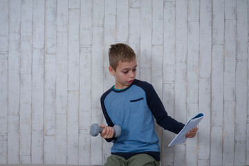 młody chłopak z ciężarkiem w dłoni czyta książkę  - obrazy, fototapety, plakaty