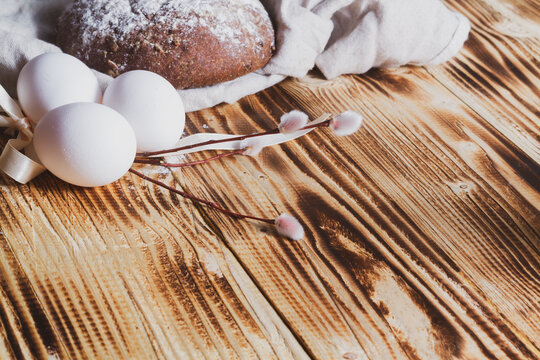 Simple Easter rustic background with a willow twig, white chicken eggs and grain bread on a brown wooden table