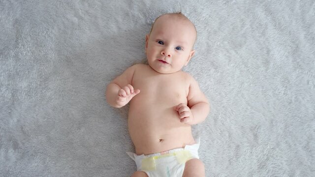 A healthy newborn baby in a nappy without clothes.  Cute baby with blue eyes . Slow motion. Happy newborn boy lies on a blue blanket and actively moves his arms and legs. Half Full  length body.
