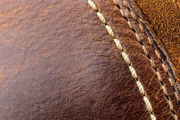 Macro background made of brown natural leather with white stitching on the right side.