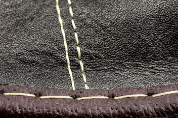 Macro background made of black natural leather with white stitching in the center.