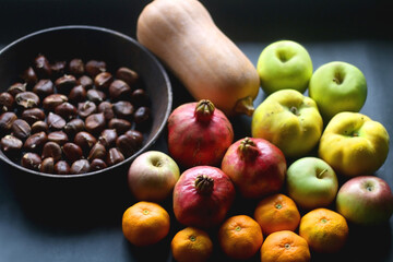 Pan with chestnuts, butternut squash and various fruit on dark background. Selective focus.
