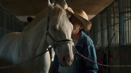 Obraz premium Elderly farmer cleaning horse in stable