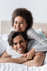 joyful interracial couple smiling while hugging on bed