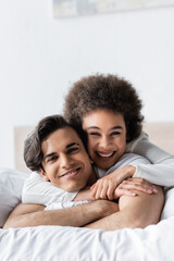 Obraz premium cheerful interracial couple smiling while hugging on bed