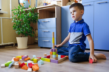 Little child, school boy playing with toy colorful wooden blocks at home. Happy family lifestyle, hobby and leisure. 