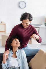 happy man holding key from new home near smiling african american girlfriend