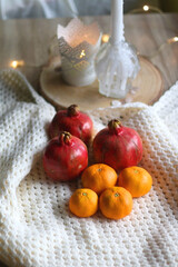 Fresh tangerines and pomegranates, soft blanket and lit candles. Selective focus.