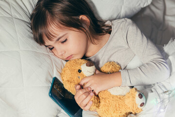 Baby little girl sleeping in bed with phone and soft teddy bear toy