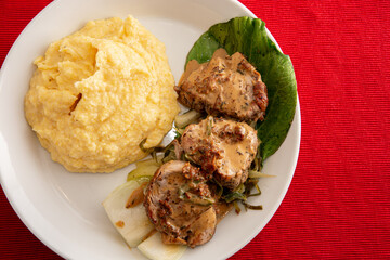 Pork medailions with polenta and pakjoi decoration from above on a white plate with a white and red background