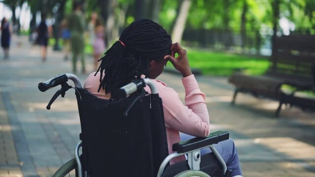Sad black woman with disability sitting in wheelchair alone in city park