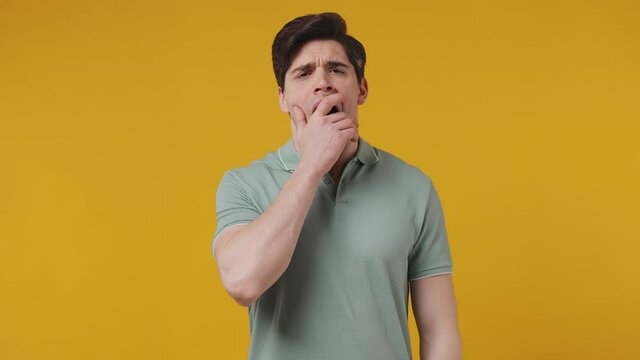 Tired sad sleepy whacked young man 20s years old wears blue t-shirt did not get enough sleep last night after party and barely got up in the morning yawning isolated on plain yellow background studio