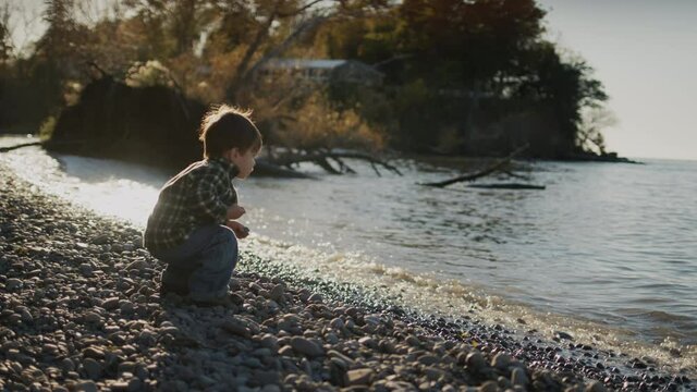 Asian kid having fun on the shore of the lake - throws stones into the water.
