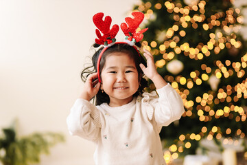 Portrait of a cheerful happy positive emotional Asian little girl the child is having fun rejoicing and holding a gift box on a Christmas holiday in a decorated house during the New Year vacation. 