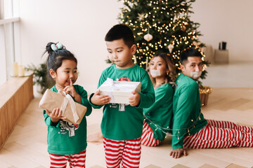 The concept of Christmas. Funny kids in green pajamas having fun tied up their parents with a rope and stole gift boxes during the New Year holidays at home. Selective focus