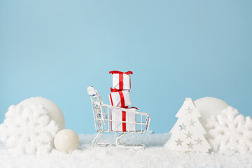Christmas gifts and shopping cart with snow around on blue background