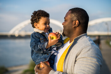 Happy father and son eating apples while spending time outdoor.