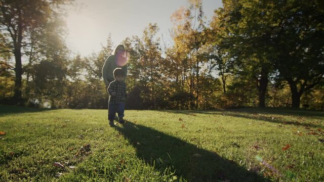 Mom runs after her baby in the meadow in the rays of the setting sun. Happy motherhood