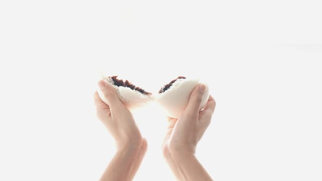 A hand that cuts the warm bread with red bean paste in half.