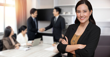 Portrait of smart and beautiful young asian businesswoman standing with confident on background of business people shaking hands after contract signing in modern office. Success business concept