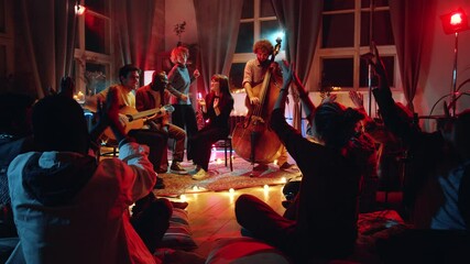 Zoom in shot of people sitting on floor in studio and applauding to young music band giving live concert