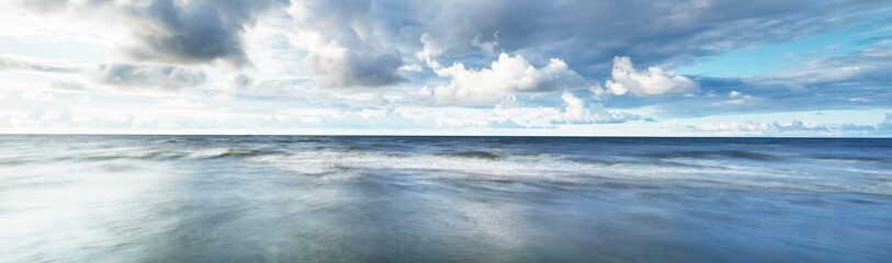 Clear sky with lots of glowing cumulus clouds above the Baltic sea shore after thunderstorm at sunset. Dramatic cloudscape. Picturesque scenery. Fickle weather, climate change. Long exposure