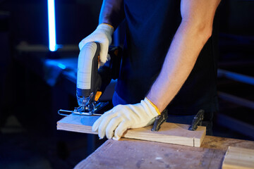 men's hands sawing wood with a jigsaw with a battery on a workbench