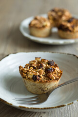 Vertical close-up of a little home-made apple pie with pieces of apple and raisins and a fork on a porcelain plate. Selective focus.