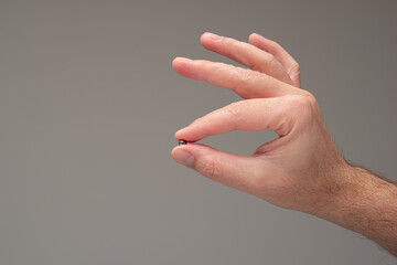 Very small metal bearing ball held between fingers by Caucasian male hand. Close up studio shot,...