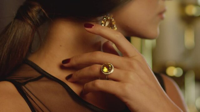 Beautiful brunette woman wearing  luxury expensive jewelry with yellow shining diamonds . Girl's hand slowly touching and caressing her beautiful white  neck and showing earring and ring . Closeup
