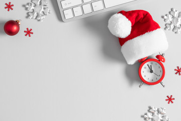 Christmas or New Year background. Office table, santa hat, christmas decorations, keyboard, alarm clock on gray table. Flat lay, top view, copy space