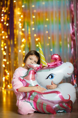 Obraz na płótnie Canvas cute girl in soft unicorn pajamas suit playing with unicorn balloon on colorful bright background, pajama theme party, rainbow theme and baby emotions