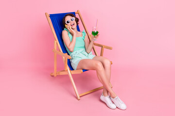 Fototapeta na wymiar Portrait of beautiful trendy cheerful girl resting in chair drinking juice talking on phone isolated over pink pastel color background
