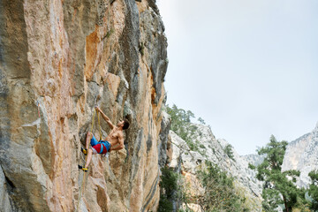 Side view muscular strong body climber man looking up, never giving up, strength and power. Sporty male feeling determined climbing on rock cliff