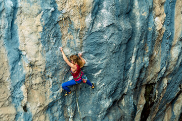 Fit athletic woman climbing on beautiful rack wall with beautiful lines and texture. Top view climber girl working out on hard route