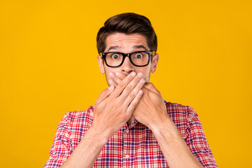 Portrait of attractive amazed worried guy geek wearing specs closing mouth oops isolated over...