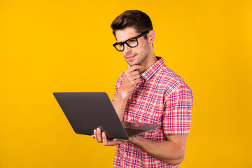 Portrait of attractive trendy focused guy geek hacker using laptop reading report isolated over bright yellow color background