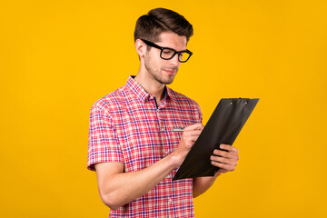 Photo of young focused serious man hold hands clip board write businessman isolated on yellow color...